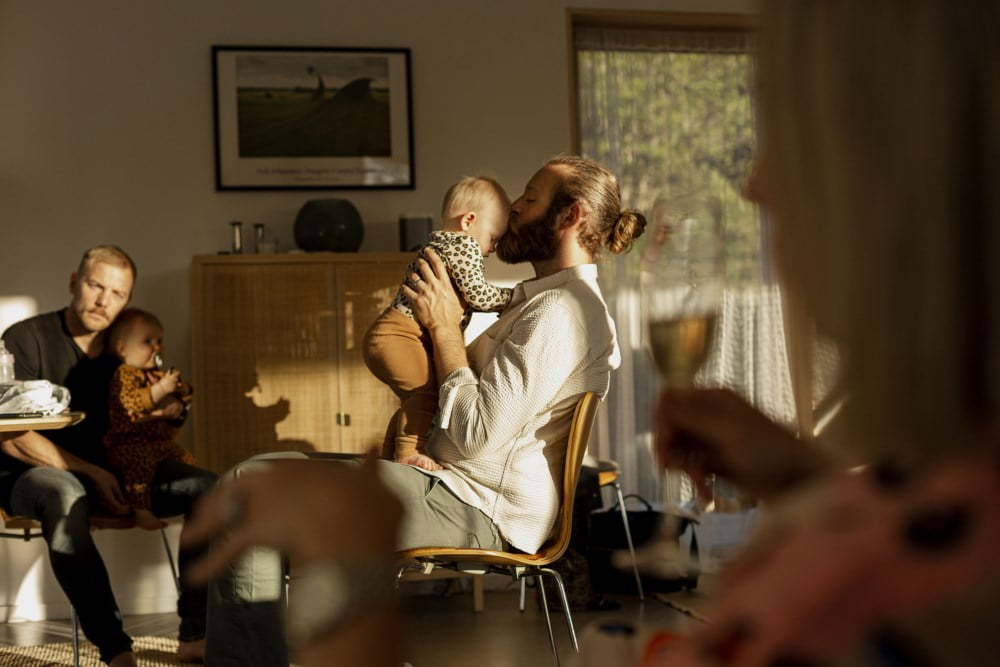 Man holder en baby i en høstlig stue, dekket av mykt lys.
